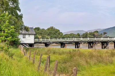 a bridge over a river with a building next to a field at Finest Retreats - Toll Bridge Cottage in Dolgellau