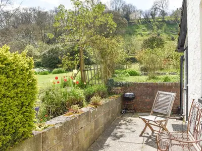a patio with chairs and a grill in a garden at Upper Broughton Farm Cottage in Snead