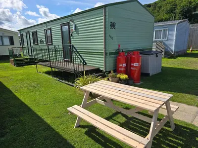 a wooden picnic table in front of a green trailer at Beautiful 2 bedroomed mobile home in Aberystwyth