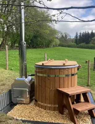 a wooden hot tub with a bench and a stove at Foxgloves and Fairytales Hut with Hot Tub in Llanwrda