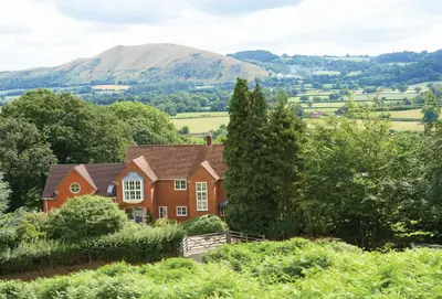 a house on a hill with mountains in the background at The Oaks in All Stretton