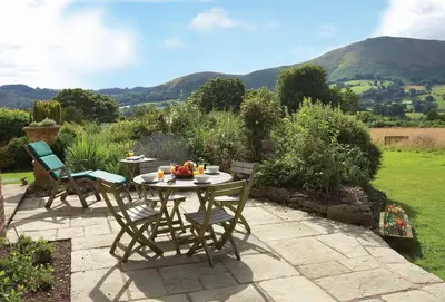 a patio with a table and chairs in a garden at The Oaks in All Stretton