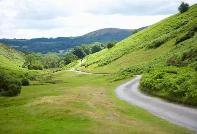 a winding road through a grassy hill with a mountain at The Oaks in All Stretton