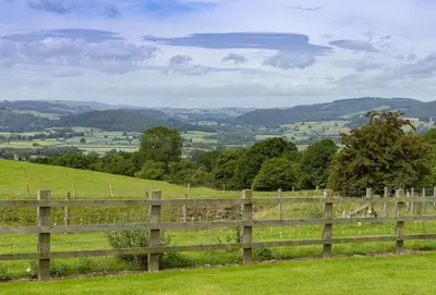 a wooden fence in a field with hills in the background at Wassell Barn in Craven Arms