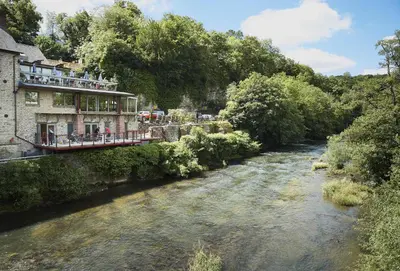 a river next to a building with people on a bridge at The Stone Barn in Downton