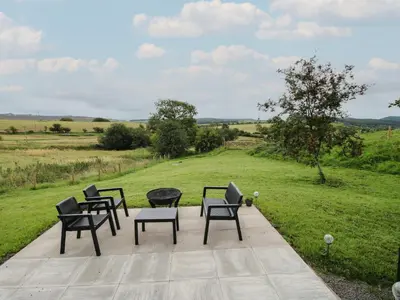 a group of chairs and tables on a patio with a field at Little Shelve Barn in Shrewsbury