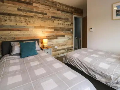 a bedroom with two beds and a wooden wall at Y Bwthyn in Llanbedr