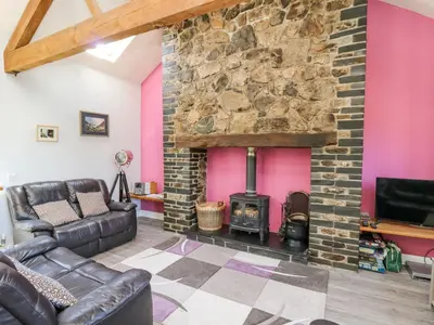 a living room with a stone fireplace and leather furniture at Swn y Nant in Tywyn