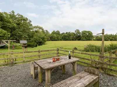 a picnic table with a bottle of wine and a field at Halls Mill in Kington