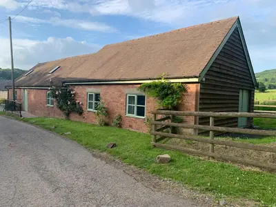 a brick house with a fence next to a road at Cow Shed in Farden