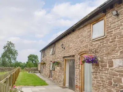 an old brick building with flowers on the door at Stoke Court Farm Barn in Stoke Saint Milborough