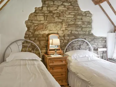 two beds in a bedroom with a stone wall at Titchbourne Cottage in Clee Saint Margaret