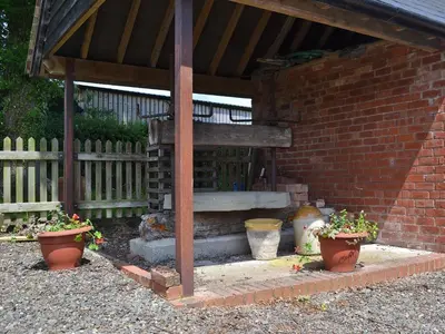 a stone bench under a pavilion with two potted plants at The Cider Mill Cottage in Orleton