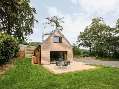 a small cabin with a patio and chairs in the yard at The Larches in Bishops Castle