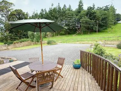 a wooden table and chairs with an umbrella on a deck at Llofft Stabal in Llanerfyl