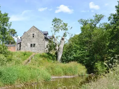 an old stone house on a hill next to a river at Ty Rhyd in Llanrhaeadr-ym-Mochnant
