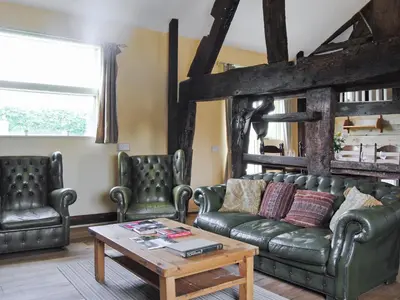 a living room with a leather couch and two chairs at Hirros Hall Longhouse in Llanerfyl