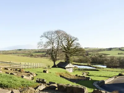 a field with a fence and a river and a house at The Farmhouse in Mydroilin