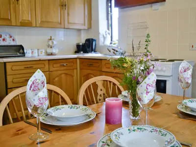 a kitchen table with plates and glasses and flowers on it at Greenmeadow Bungalow in Llanon
