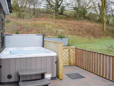 a hot tub on a deck with a wooden fence at Beudy Bach-Oh5 in Dihewid
