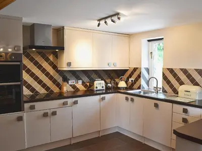 a kitchen with white cabinets and black counter tops at Beudy Bach-Oh5 in Dihewid