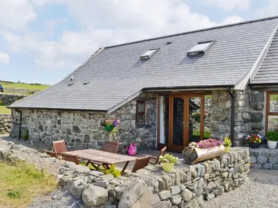 a stone cottage with a wooden table and chairs at Beudy Hen in Harlech