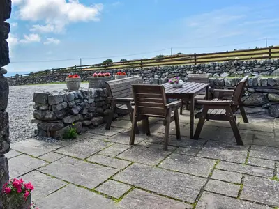a table and chairs on a patio with a stone wall at Beudy Hen in Harlech