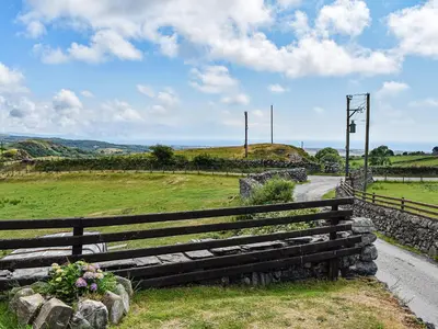 a wooden fence next to a road in a field at Beudy Hen in Harlech