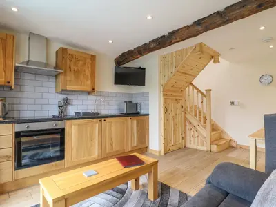 a kitchen with wooden cabinets and a living room at Old Cart House in Oswestry