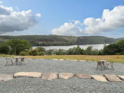 a group of tables and chairs on a gravel area with a lake at Old Cart House in Oswestry