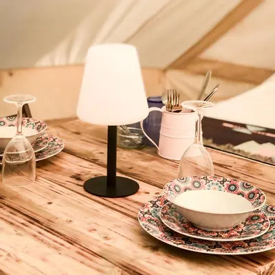 a wooden table with plates and a lamp on it at Tinker the Bell Tent at Pentref Luxury Camping in Penuwch
