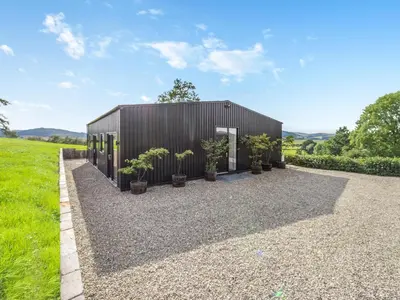 a black building with potted plants on a gravel driveway at Jacobs Plock in Leintwardine