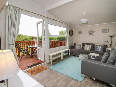 a living room with a couch and a balcony at Chalet 64 in Tywyn