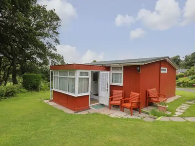 a red tiny house with chairs in the yard at Chalet 64 in Tywyn