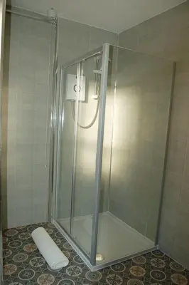 a shower with a glass door in a bathroom at Angorfa family holiday home with games room in Tywyn