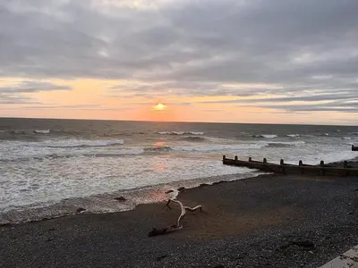 a stick on the beach with the sunset in the ocean at Angorfa family holiday home with games room in Tywyn