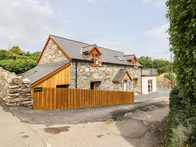 a stone house with a wooden fence in front of it at Llys Tirion in Bala