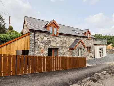 a stone cottage with a wooden fence at Llys Tirion in Bala