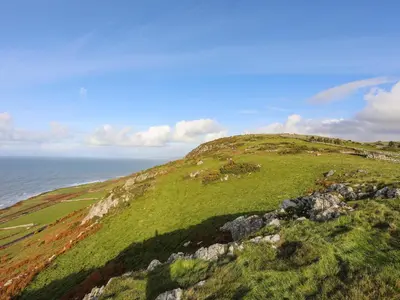 a green hill with the ocean in the background at Bryn Y Mor in Tywyn