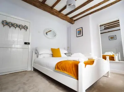 a white bedroom with a white bed with orange sheets at Characterful 3 Bedroom Cottage in Aberystwyth