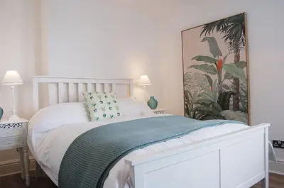a bedroom with a white bed and a painting on the wall at Driftwood Designer Apartment in Tywyn