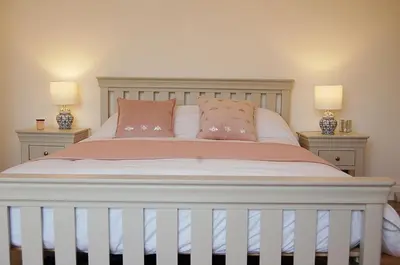 a white bed with pink pillows and two lamps at Driftwood Designer Apartment in Tywyn