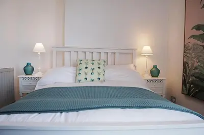 a bedroom with a white bed with two lamps at Driftwood Designer Apartment in Tywyn