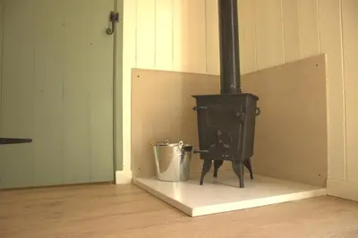 a black stove with a bucket in a room at Cosy Shepherd's Hut with Hot Tub in Church Stretton
