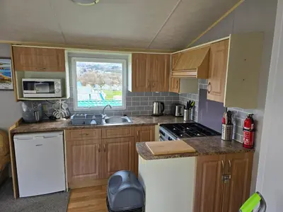 a small kitchen with wooden cabinets and a window at Light and Airy 2 Bedroom Mobile Home in Aberystwyth