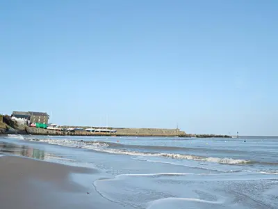 a beach with the ocean and a pier in the background at Maesyrhaf in Llanllwchaiarn