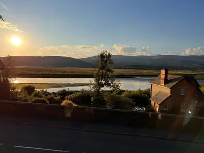 a view of a house and a river with the sun at Penestaer in Machynlleth