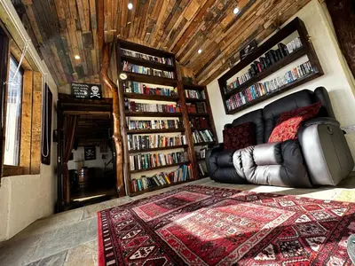 a living room with a couch and book shelves with books at Coed Y Ddraig - themed 3 bedroom cottage, with bar & pool table in Tregaron