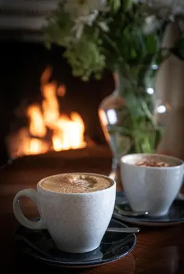 two cups of coffee on a table with a fireplace at Caer Beris Manor By Group Retreats in Builth Wells