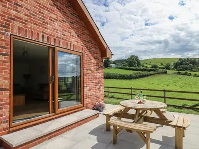 a patio with a table and bench and a brick building at Awel y Bryn in Rhayader
